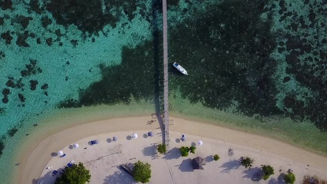 Beautiful aerial landscape footage of wooden pier at Kanawa Island Resort with turquoise water and boats in East Nusa Tenggara, Indonesia. Shot in 4k resolution