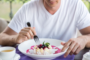 Handsome young man eating with a fork cake Pavlova