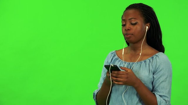 A young black woman listens to music on a smartphone - green screen studio