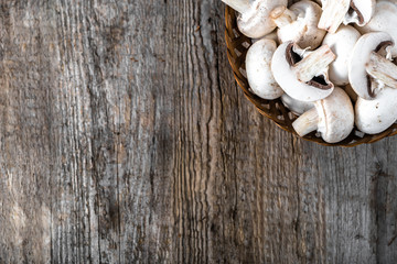 Fresh champignon mushrooms in a basket on wooden table, overhead