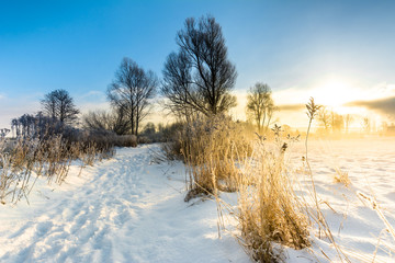 Sunset winter landscape with road in snow and blue sky with sun illumination