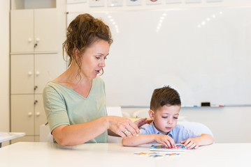 teacher woman and preschooler boy playing with puzzle game in the classroom