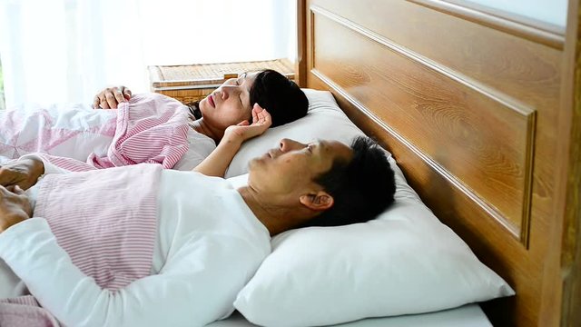 Woman snoring loud and choking,waking her husband up during the night,he pushing her to sleep on his side.People who snore with choking sound symptom called obstructive sleep apnea,healthcare concept.