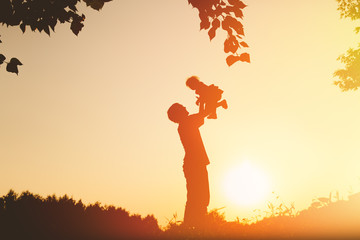Father and little baby silhouettes play at sunset