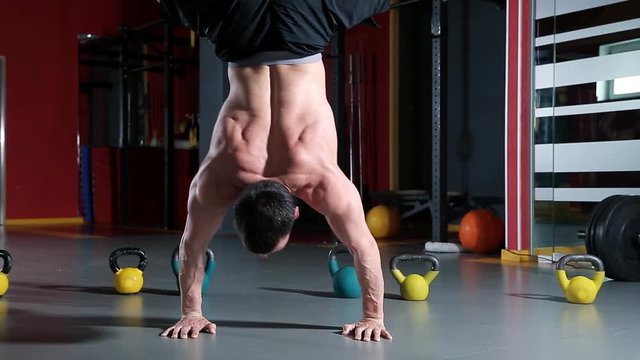 Athlete with naked torso doing push-ups on his hands while standing upside down