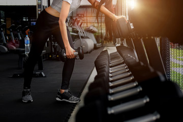 Fototapeta na wymiar Fit woman wearing sports clothes weighing dumbbells in hands during workout in modern gym.
