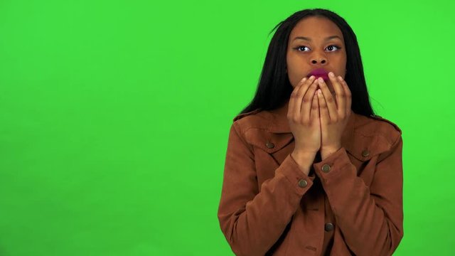 A young black woman covers her eyes with her hands, stops and looks around in confusion - green screen studio