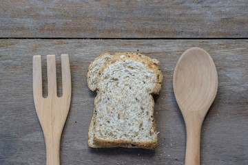 slice of fresh organic whole wheat bread on the old wood background with wooden spoon and fork.