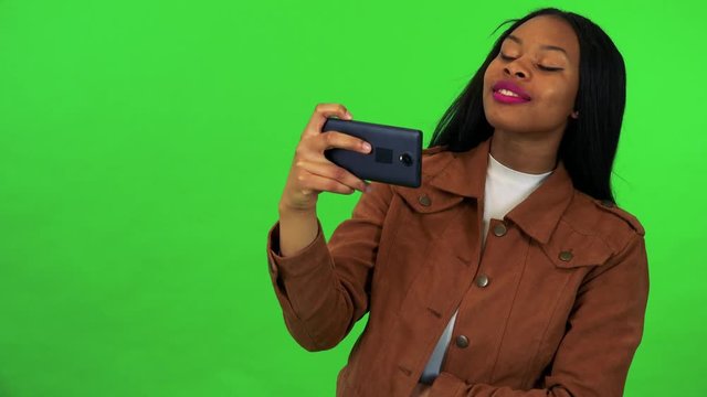 A young black woman takes pictures of something off the camera with a smartphone - green screen studio