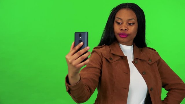 A young black woman takes selfies with a smartphone - green screen studio