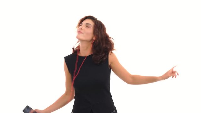 Joyful young girl in black dress listening to the music with her earphones and having fun dancing isolated on the white background