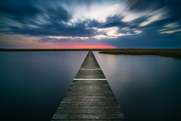 Old wooden pier on calm lake at sunset
