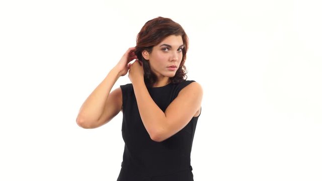 Attractive young woman is tiding her hair looking in the camera like in the mirror and asking for advice standing isolated on a white background. Woman's hairdo