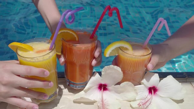 Hands put three glasses of freshly squeezed natural juice with straws and pieces of fruit on the edge of the pool at the resort. 4k