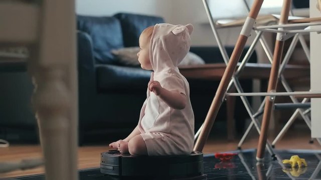 Little baby girl sitting on robot vacuum cleaner while cleaning house