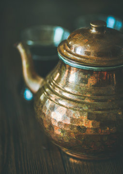 Oriental Middle Eastern vintage copper hummered tea pot and black tea in traditional tulip glasses over rustic wooden background, selective focus