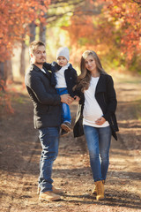 Fototapeta premium Young happy family have fun and walking in the autumn park. Pregnant woman with husband and little son