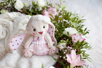 Teddy Rabbit toy on a on knitted plaid. Handmade stylish beautiful toy with flowers