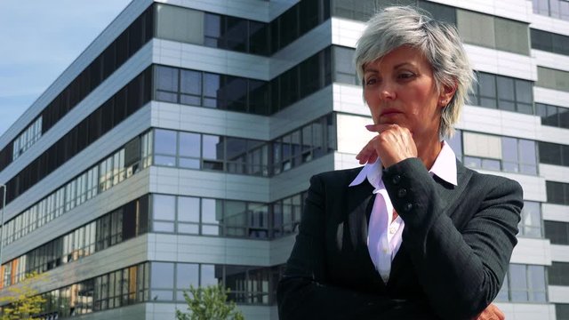 Business middle age woman thinks about something - company building in the background 