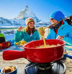 Swiss fondue dinner family skiers enjoying break for lunch, mountain view Matterhorn, Switzerland. - obrazy, fototapety, plakaty