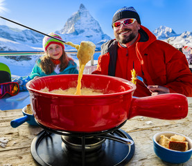 Swiss fondue dinner family skiers enjoying break for lunch, mountain view Matterhorn, Switzerland.