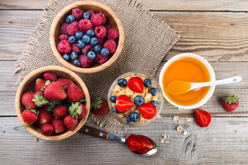 Healthy breakfast,  flasks, berries and honey on rustic wooden background, top view