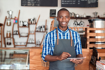 Smiling entrepreneur standing in his cafe using a digital tablet