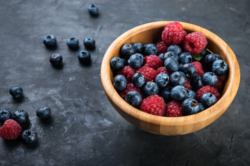  fresh blueberries and raspberries on wooden bowl in a dark background