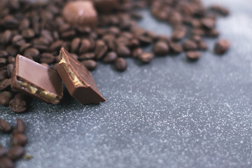 Coffee beans and tiles of dark chocolate on a dark matte background.