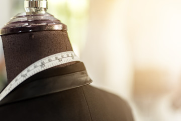 Closed up of Business black suit tailoring on tailor shop mannequin with measure tape across neck,...