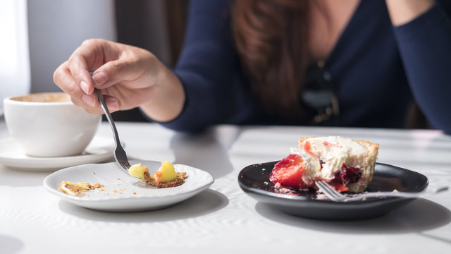 Closeup image of a woman using fork to cutting sweet dessert in a plate with white cup of coffee on vintage wooden table in cafe