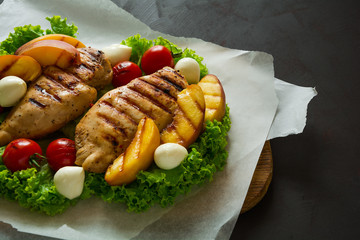 BBQ: grilled chicken breast, tomatoes,peach slices and mini mozzarella on wooden desk. Vibrant colors