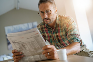Handsome mature man at home reading newspaper