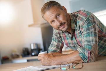 Smiling mature man drinking coffee and reading newspaper