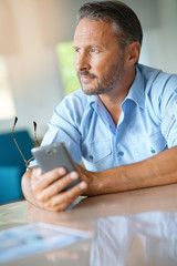 Mature man being thoughtful looking at message on smartphone