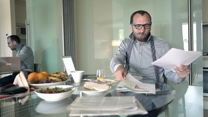 Young businessman eating breakfast and working with documents at home
 - Powered by Adobe