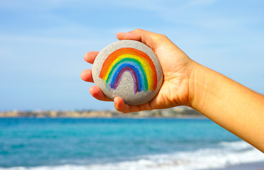 Woman hand holding pebble with painted rainbow