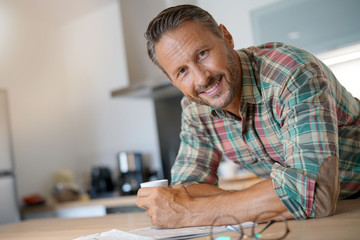 Smiling mature man drinking coffee and reading newspaper - Powered by Adobe