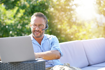 Cool businessman working with laptop and headset outside the office