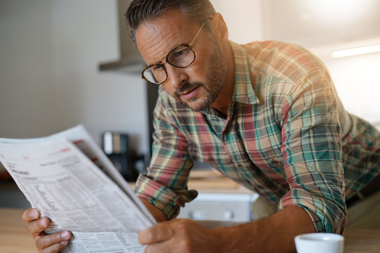 Handsome mature man at home reading newspaper