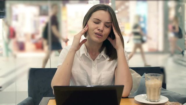 Young businesswoman having head pain during work on laptop in cafe by window
