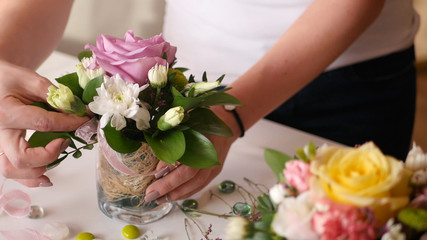 Florist girl collects a nice little bouquet of roses and other flowers in a small vase