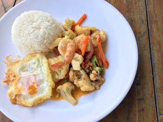 stir-fry vegetables with bean curd and shrimp in white dish with rice and fried egg on wooden background. Thai style Food.
