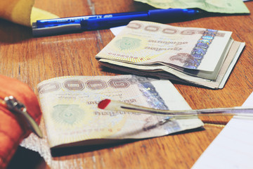 Calculator and money thai banknote with  white notebook paper, pen on wooden table at home office. The concept of financial planning, savings. vintage tone colour and motion blur moving of hand.