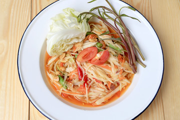 Papaya Salad with Carrot, Lentils, Tomato, Dried Shrimp, Chilli, in a White plate on wooden background. Thai style food.
