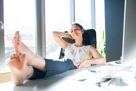 Businesswoman in her office sitting with legs on desk.