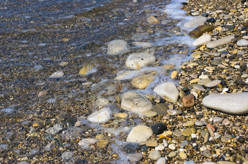 sea pebble beach with multicoloured stones, waves with foam