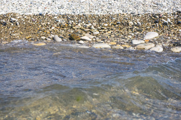 sea pebble beach with multicoloured stones, waves with foam
