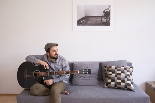 A young man is rehearsing on a bass guitar sitting in a couch