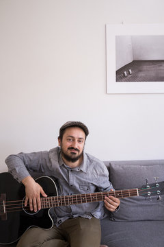 A young man is rehearsing on a bass guitar sitting in a couch